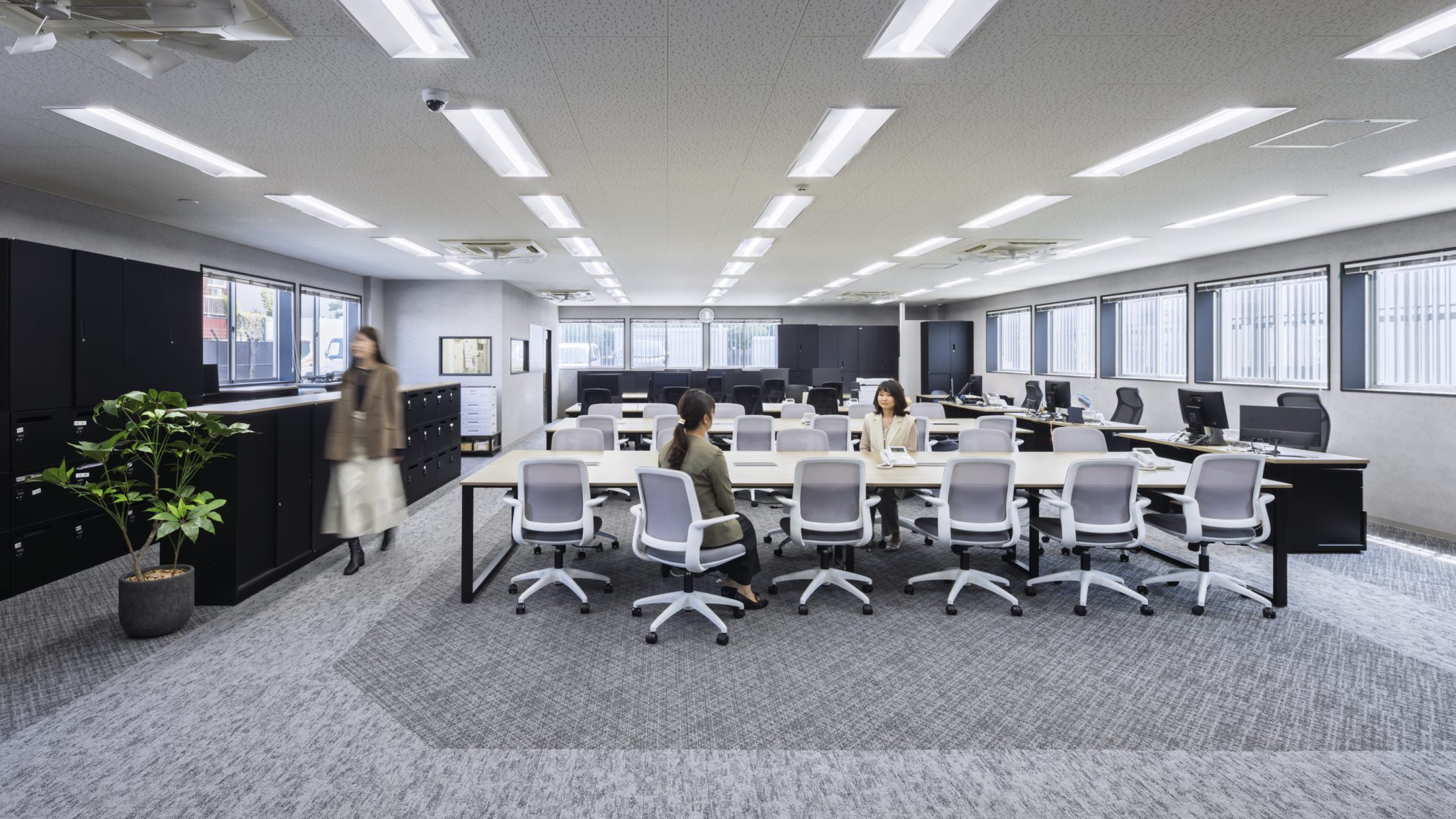 TSネットワーク株式会社 泉大津流通センター １階執務室。グレー系のカーペットとブラックの什器でまとめたシックな執務空間。広い窓から自然光が差し込み、集中しやすい落ち着いた環境を実現している。